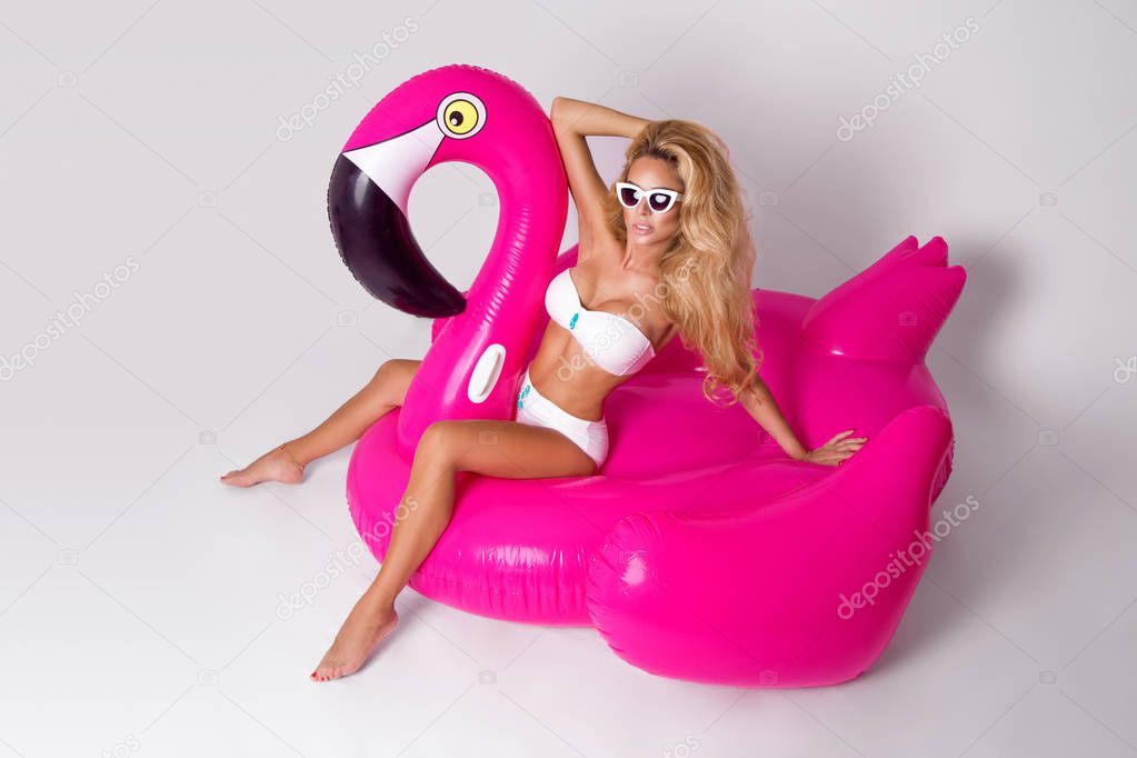 Beautiful, sexy blonde model in a elegant bikini, lies on a pink flamingo. Hit the summer