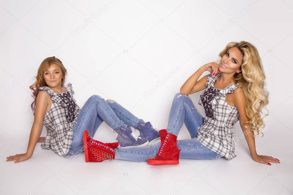 Beautiful blond girls, mother with daughter in jeans clothing on a white background in the studio.
