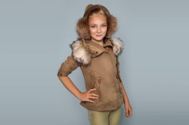 Sevimli küçük kız kış giysileri giymiş şapka ve kış ceket, üzerinde mavi arka plan ayakta