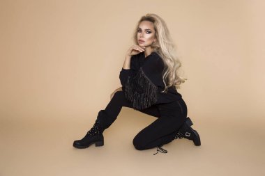 Güzel, Genç kadın modelinde bir sonbahar-kış giyim, askeri hoodie ve tulum ve bej renkli bir arka plan stüdyo bot. Sarışın şık motorcu, askeri tarzı giyim