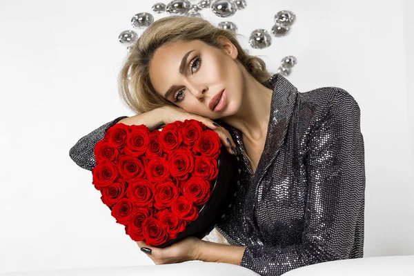 Valentine Beauty girl with red heart roses. Portrait of a young female model with gift, isolated on background. Beautiful Happy Young woman presenting products. Holiday party, birthday. Joyful model