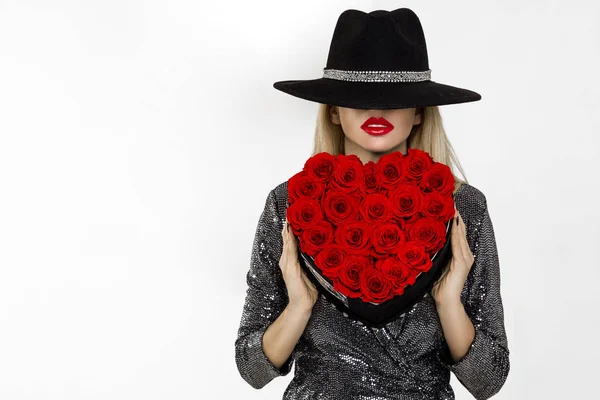 Valentine Beauty girl with red heart roses. Portrait of a young female model with gift and hat, isolated on background. Beautiful Happy Young woman presenting flower box. Holiday party, birthday.