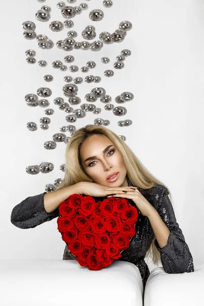 Valentine Beauty girl with red heart roses. Portrait of a young female model with gift, isolated on background. Beautiful Happy Young woman presenting products. Holiday party, birthday. Joyful model