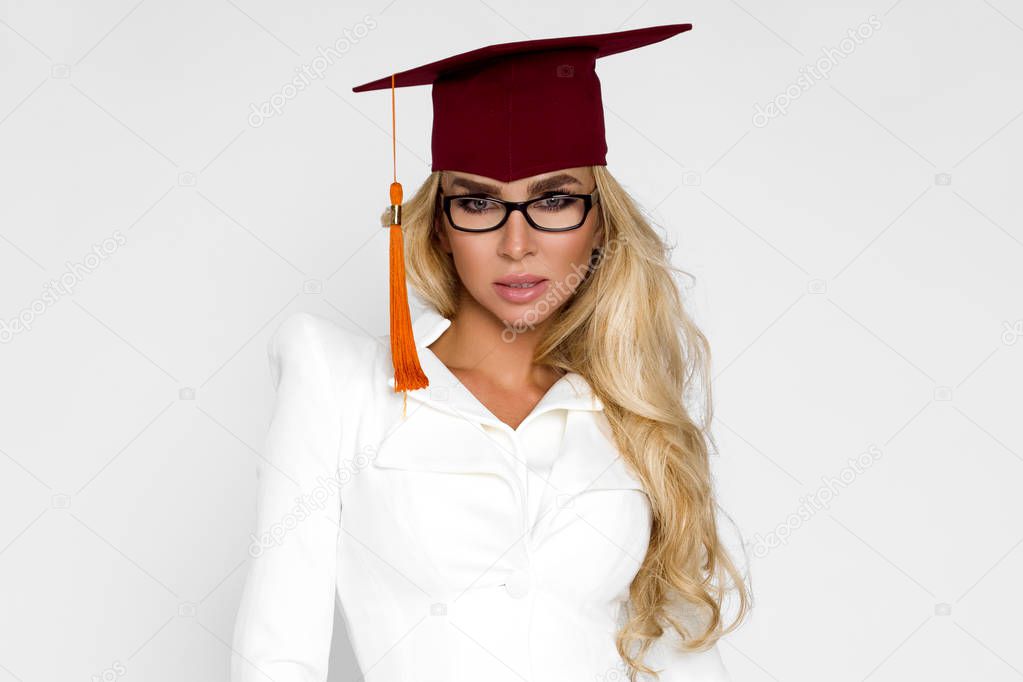 Beautiful girl in gratuate outfit is standing on the white background in the studio, in the mantle. She is a graduate. She is glad. She's in a good mood. - Image