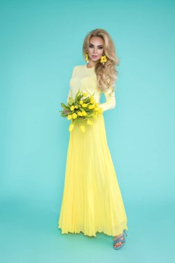 Bahar kadın. Bir buket bahar çiçek tutan güzellik yaz modeli kız renkli giysileri ile. Bu güzel hanımla mavi zemin üzerine Sarı laleler.