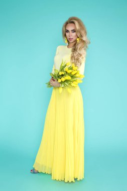 Bahar kadın. Bir buket bahar çiçek tutan güzellik yaz modeli kız renkli giysileri ile. Bu güzel hanımla mavi zemin üzerine Sarı laleler.