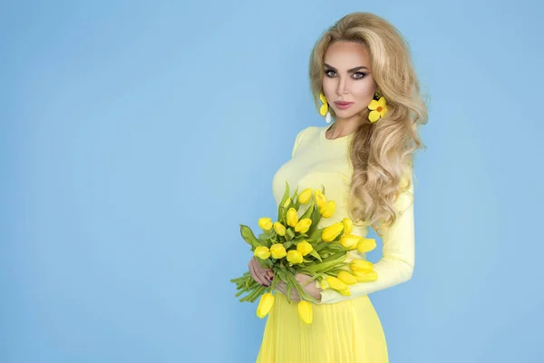 春の女性 夏モデル美少女カラフルな服を着て 春の花のブーケを保持しています 青い背景に黄色のチューリップを持つ美しい女性 — ストック写真
