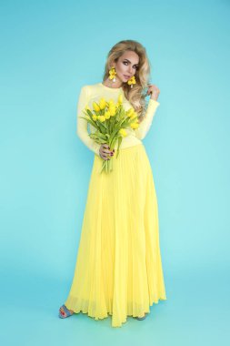 Bahar kadın. Bir buket bahar çiçek tutan güzellik yaz modeli kız renkli giysileri ile. Bu güzel hanımla mavi zemin üzerine Sarı laleler.