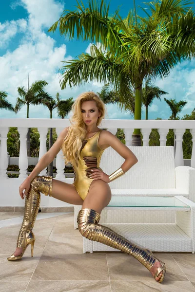 Beautiful sexy woman in gold bikini and gold shoes posing on the caribbean luxury hotel.