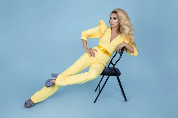 スタイリッシュな黄色のジャンプスーツと色の背景にファッショナブルなアクセサリーでエレガントなブロンドの女性 青い背景に美しいファッションモデル — ストック写真