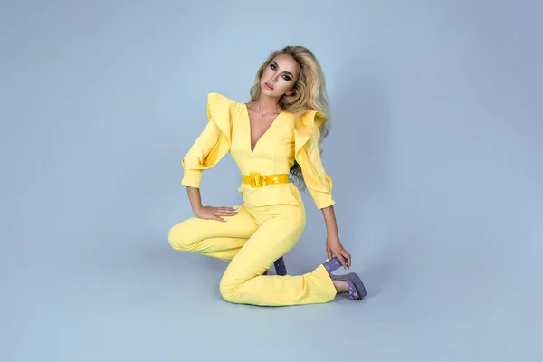 优雅的金发女人在时尚的黄色连身衣和时尚的配件的颜色背景 蓝色背景上美丽的时尚模型 — 图库照片