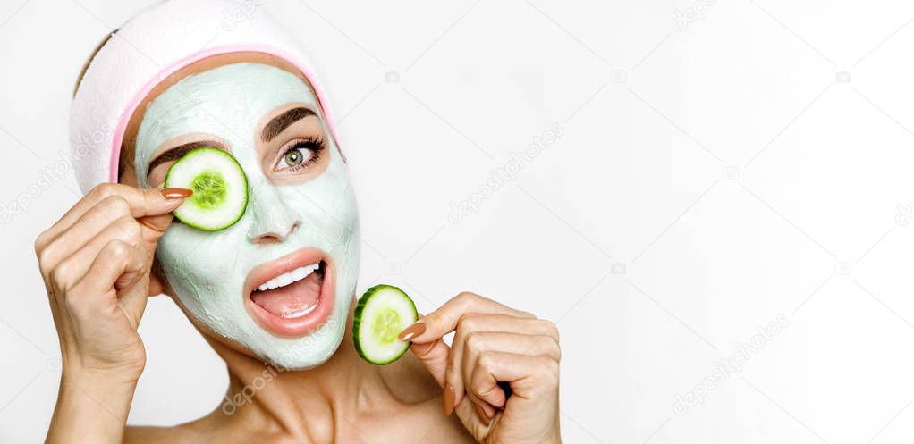 Young smiling woman with a clay mask. Photo of attractive young woman covering her eyes with cucumbers on a white background. Grooming himself - Image
