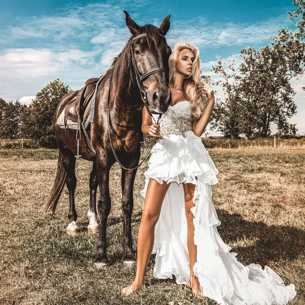 Portrait of a dark horse and woman. Beautiful glamour woman with a horse. Portrait of a beauty blonde bride in wedding dress with horse.