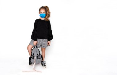 Coronavirus covid-19 virüsü. Okul konseptine geri dönelim. Coronavirus sırasında sırt çantalı ve cerrahi maskeli şirin bir kız çocuğu okula giderken beyazlar içinde izole edilmiş.