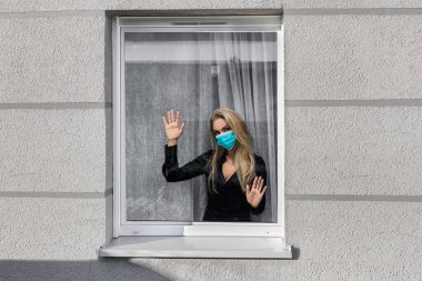 Coronavirus. Corona virüsünün hasta kadını pencereden dışarı bakıyor ve maske takıyor ve evdeki hastalıktan korunuyor. Karantinaya alın. Hasta enfeksiyonu önlemek için izole edildi.