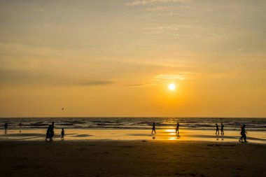 Goa, Hindistan 'da deniz kıyısında yürüyen insanların siluetleri. 
