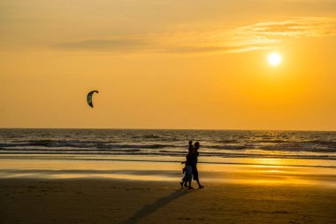 Goa, Hindistan 'da deniz kıyısında yürüyen insanların siluetleri. 