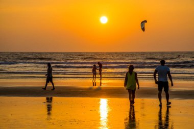 Goa, Hindistan 'da deniz kıyısında yürüyen insanların siluetleri. 