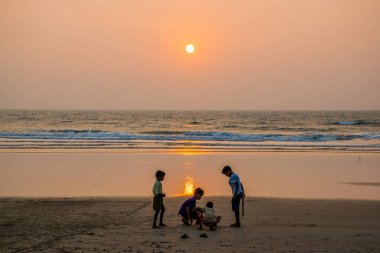 Goa, Hindistan 'da deniz kıyısında yürüyen insanların siluetleri. 