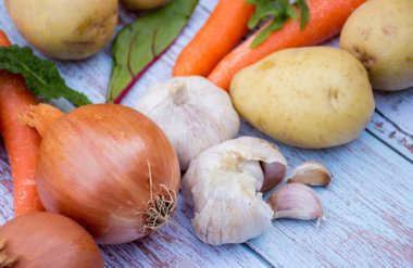 Olgun havuç, patates, sarımsak, salata yaprakları ve ahşap masa arka plan üzerinde kahverengi soğan. Pişirme malzemeleri. Hasat.