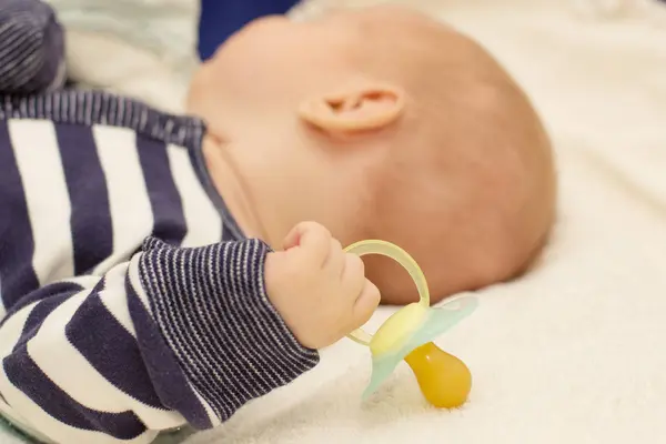 Little baby boy is peacefully sleeping and holding a pacifier dummy in his hand. — Stock Photo, Image