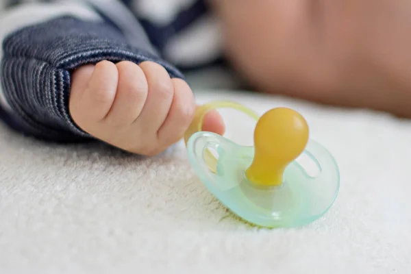 Little baby boy is peacefully sleeping and holding a pacifier dummy in his hand. Selective focus on a dummy — Stock Photo, Image