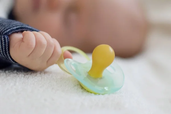 Little baby boy is peacefully sleeping and holding a pacifier dummy in his hand. Selective focus on a dummy — Stock Photo, Image