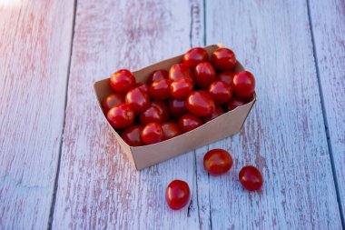 Organik olgun kiraz domates ahşap bir masa üzerinde geri dönüşümlü kağıt kutusunda. Pişirme malzemeleri. Hasat. Sürdürülebilir yaşam. Plastik ambalajlara hayır deyin.