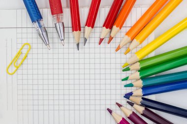 Geri okul kavramı - gökkuşağı kalemler, jel kalemler, bağlayıcı ataş ve ızgara kağıt defter backgorund ataş. Metin girişi için boş alan.