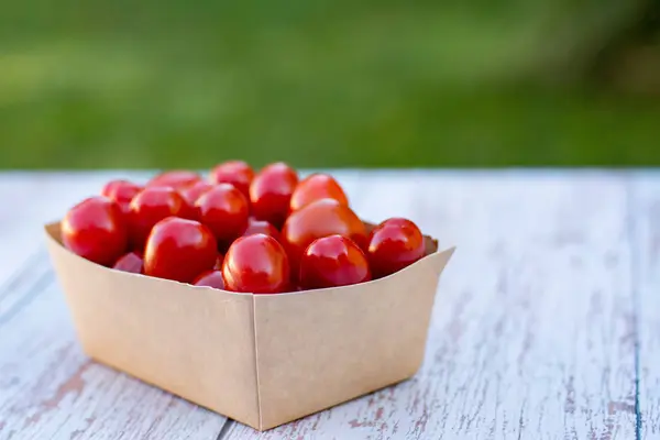 Tomates cereja maduros orgânicos em uma caixa de papel reciclável em uma mesa de madeirano jardim. Cozinhar ingredientes. Colheita. Vida sustentável. Diga não à embalagem de plástico . — Fotografia de Stock