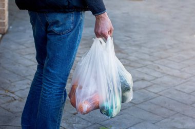Adam yürüyüş ve çeşitli meyve ve bakkaliye ile plastik alışveriş torbaları tutarak. Çevre kirliliği, atık sorunu, çöp, çöp.