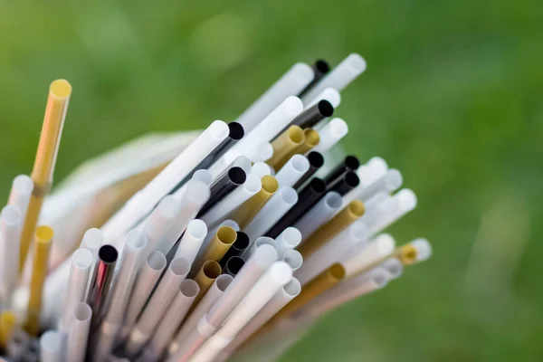 Plastic straws in a plastic bag on green grass background. Plastic pollution, environmental waste. Say no to plastic straws. Save our green planettic