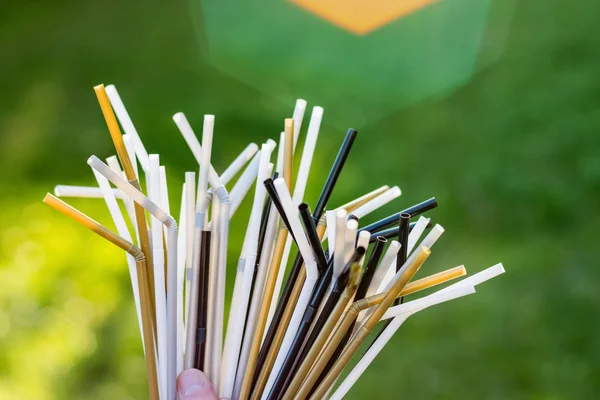 Hands holding plastic straws on green grass background. Plastic pollution, environmental waste. Plastic pollution, environmental waste. Say no to plastic straws. Save our green planettic