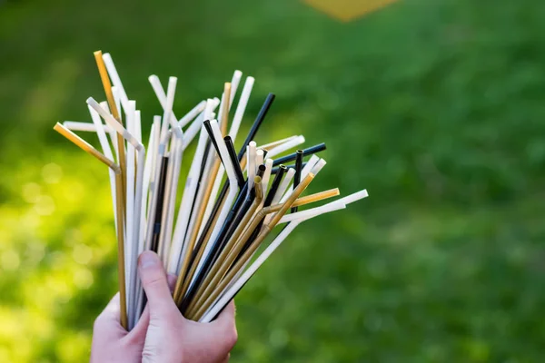Hands holding plastic straws on green grass background. Plastic pollution, environmental waste. Plastic pollution, environmental waste. Say no to plastic straws. Save our green planettic
