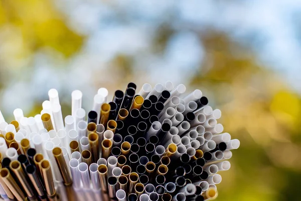 Heap of white, black ang gold plastic straws on nature background. Plastic pollution, environmental waste. Say no to plastic