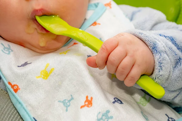 Bebê segura uma colher e colocá-lo em sua boca com sua mãozinha. Bebê primeiro soilds. Desmame . — Fotografia de Stock