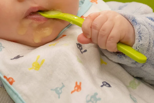 Bebê segura uma colher e colocá-lo em sua boca com sua mãozinha. Bebê primeiro soilds. Desmame . — Fotografia de Stock