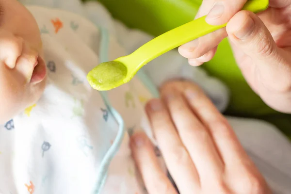 Adulto alimenta pequeno purê de brócolis bebê com uma colher. Bebê primeiro soilds. Desmame . — Fotografia de Stock