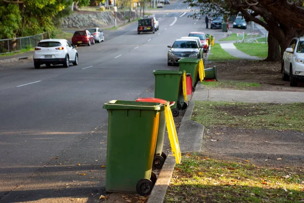 Australian garbage wheelie bins with colourful lids for recycling and general household waste lined up on the street kerbside for council rubbish collection. Parking issues.