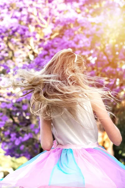 Дівчина з довгим світлим волоссям біля джакарди в повному розквіті з красивими фіолетовими квітами — стокове фото