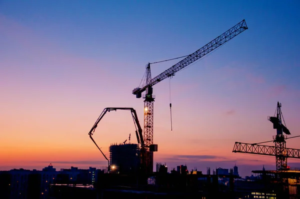 Industrial construction cranes and building silhouettes at sunrise or sunset. Urban city development