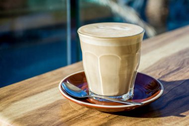 Bir bardak kahve ve bir kaşık tahtadan bir masada kahverengi bir tabakta..