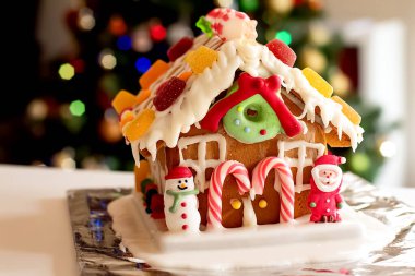 Krema, şeker, biblo, lolipop ve arkaplanda bulanık Noel ağacı olan şeker kamışlarıyla süslenmiş ev yapımı zencefilli kurabiye evi..