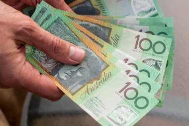 Avustralya dolarlarıyla el ele tutuşurken cam masa arkasında 100 banknot. Finans ve ödeme kavramı.