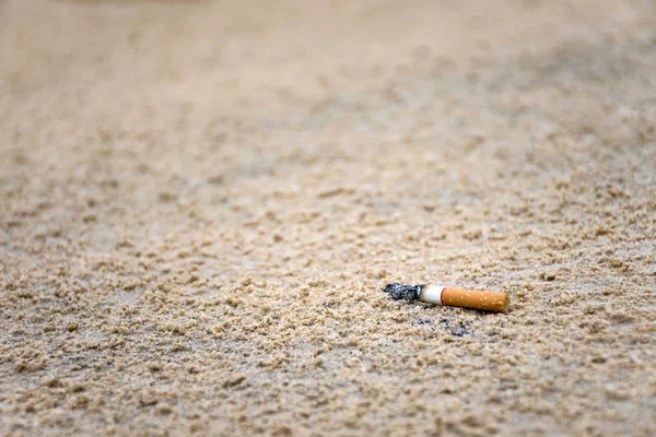 Lanzamiento de cigarrillos en la arena por humanos en la playa es causa de la basura en el océano y la contaminación ambiental . — Foto de Stock