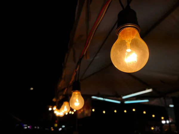 Orange electric lamp hanging on tent at Street night market.