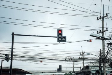 Elektrik direği üzerindeki Elektrik kabloları ve Iletişim tellerinin düğümü ile kırmızı ışık gösteren kavşak yollarında trafik ışığı.