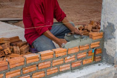İnşaat işçisi dış duvarlar için çimentoya tuğla yerleştiriyor..