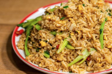 Kızarmış pirinç, yumurta ve sebzeyle karıştırılmış beyaz ve kırmızı tabak da ahşap masada..