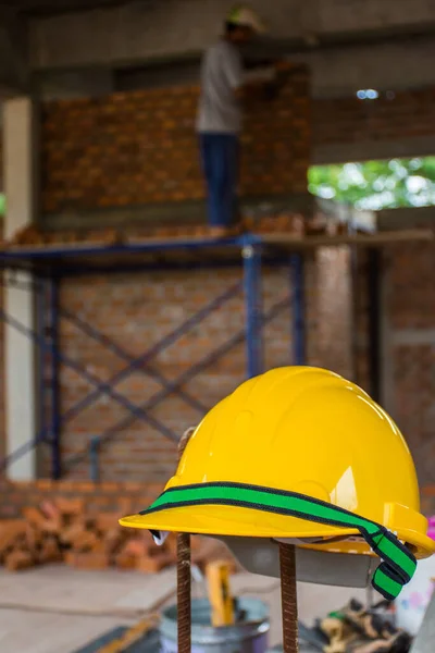 Yellow safety helmet with construction worker placing bricks on cement for building exterior walls.